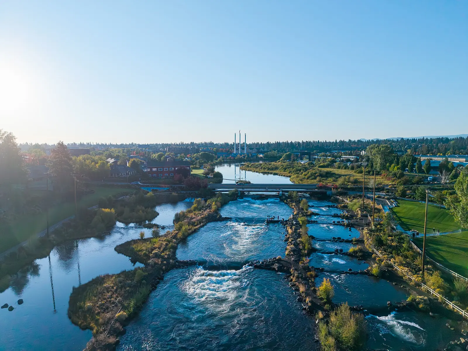 Aerial view of the Bend Whitewater Park on the Deschutes with the Old Mill smokestacks behind