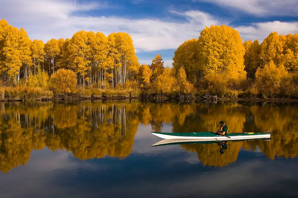 A kayaker on a glassy stretch of the Deschutes River lined with golden aspens near Dillon Falls
