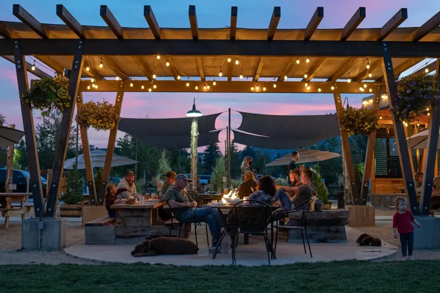 People around a fire pit under the pergola at On Tap in Bend at dusk