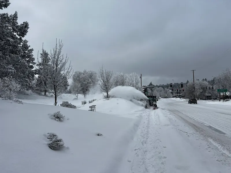 A crew blowing deep snow off a sidewalk along a Bend street with frosted trees