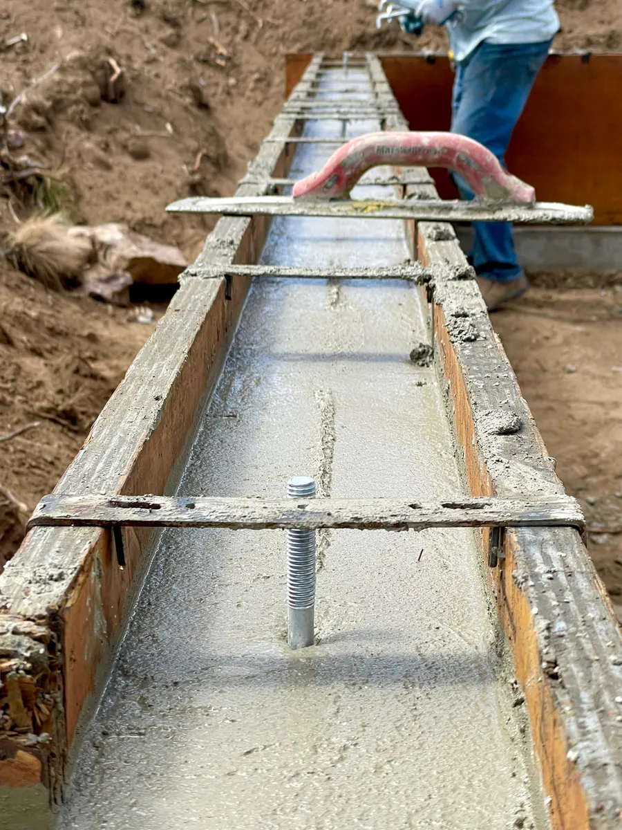 A freshly poured concrete footing in wood forms with a steel anchor bolt set in it