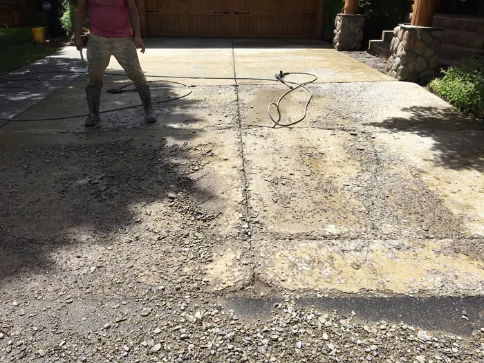 A worker pressure-washing a worn, pitted concrete driveway before resurfacing
