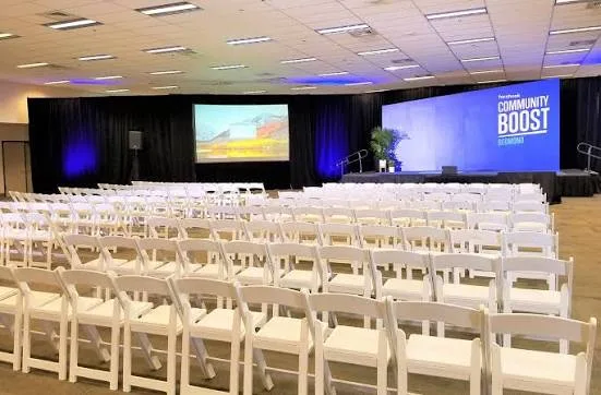 Rows of white chairs facing a stage and screens in a hall at the Deschutes County Fair & Expo Center