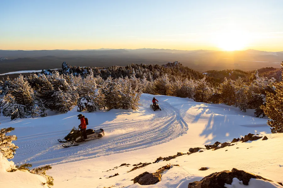 A snowmobiler on a snowy ridge at sunrise with Octane Adventures near Bend