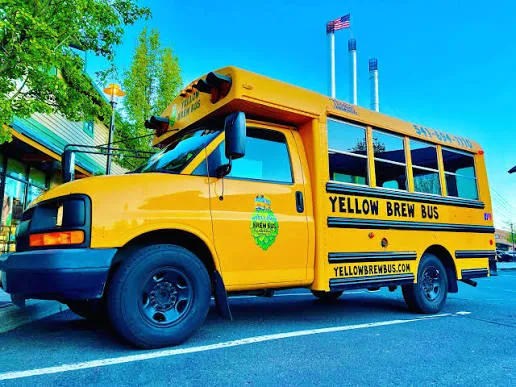 The Yellow Brew Bus parked in Bend with the Old Mill smokestacks behind it