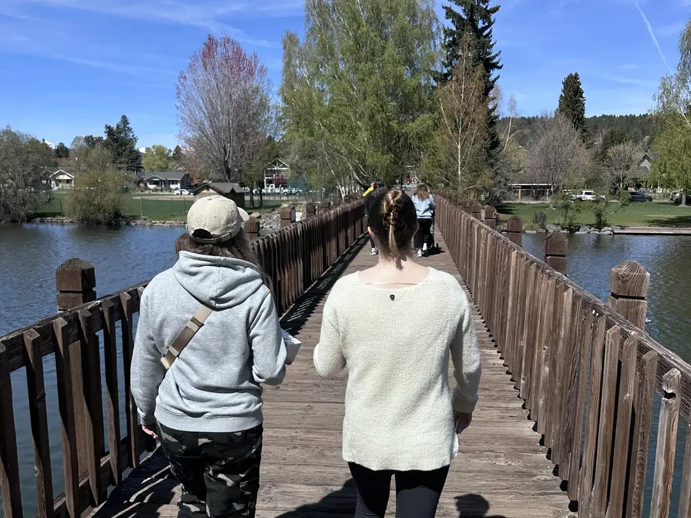 Two people walking across the wooden footbridge at Drake Park in downtown Bend