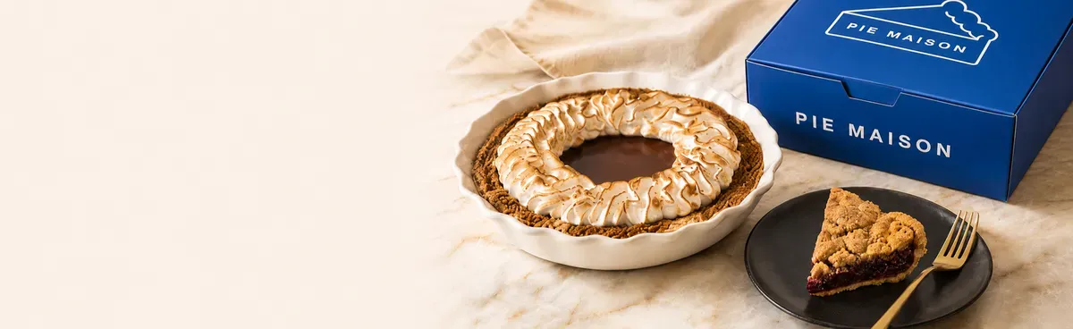 A slice of pie on a plate next to a Pie Maison pie box