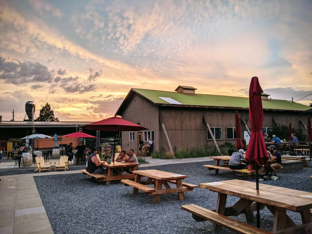People at picnic tables on the patio at Bevel Craft Brewing in Bend at sunset