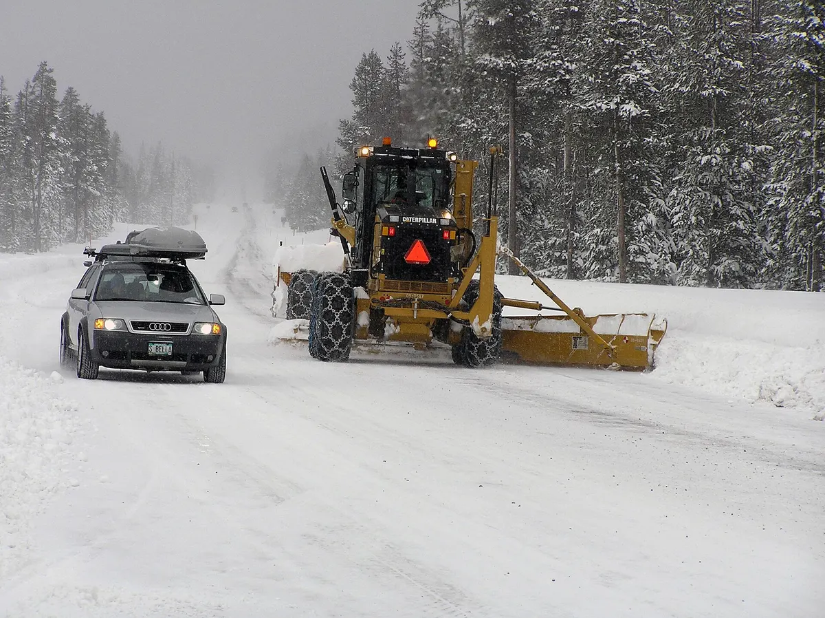 A station wagon with a roof cargo box drives past an ODOT road grader clearing deep snow on Century Drive west of Bend