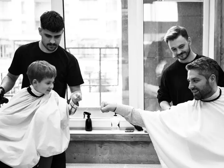 Barbers at West Side Barbershop fist-bumping a young client after a haircut