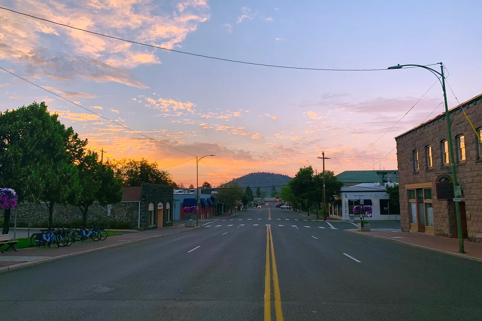 Early morning on a quiet downtown Bend street lined with brick and stone storefronts, with Pilot Butte at the end of the road