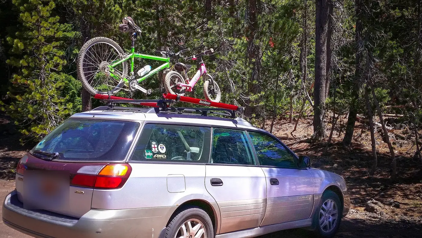 A silver Subaru wagon with two bikes on a red roof rack, parked among pines in the Deschutes National Forest