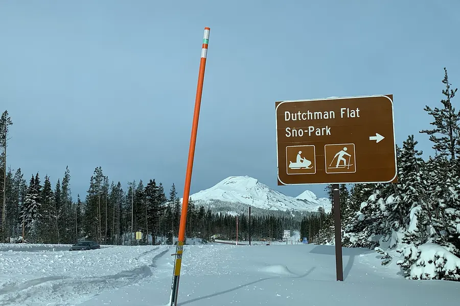Dutchman Flat Sno-Park sign beside a snowy lot with Mt. Bachelor behind