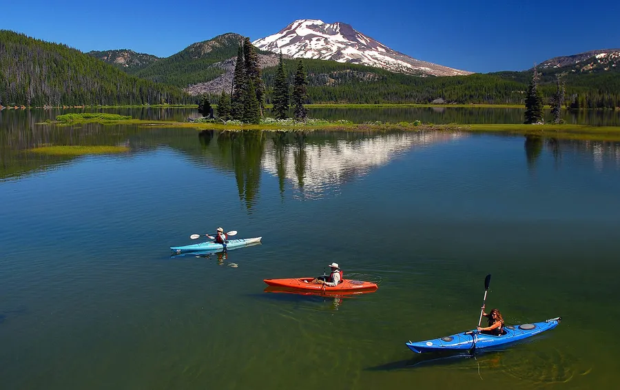 Three kayakers in red and blue boats on Sparks Lake with snowy South Sister behind