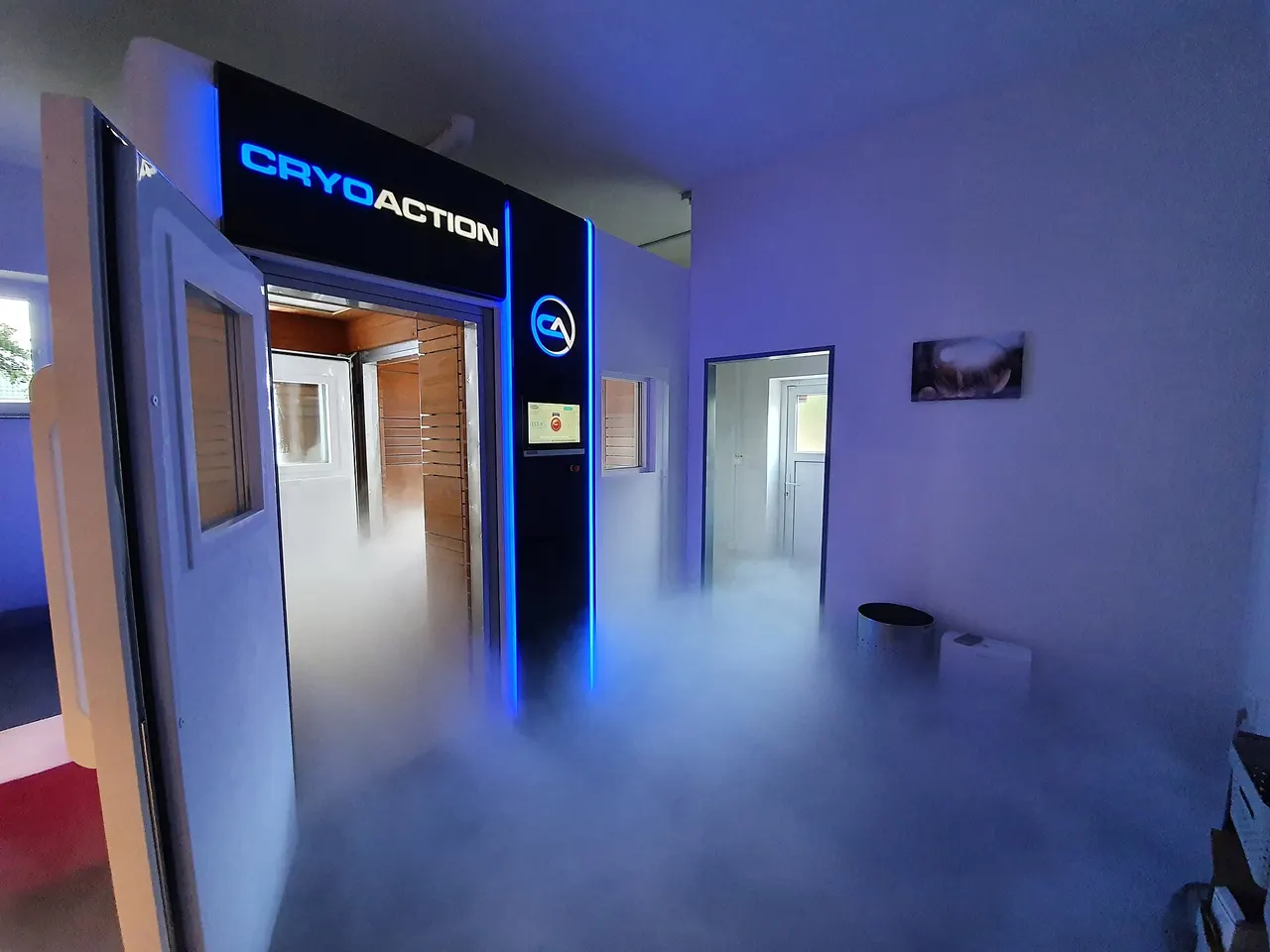A walk-in whole-body cryotherapy chamber with blue lights and cold vapor spilling across the floor