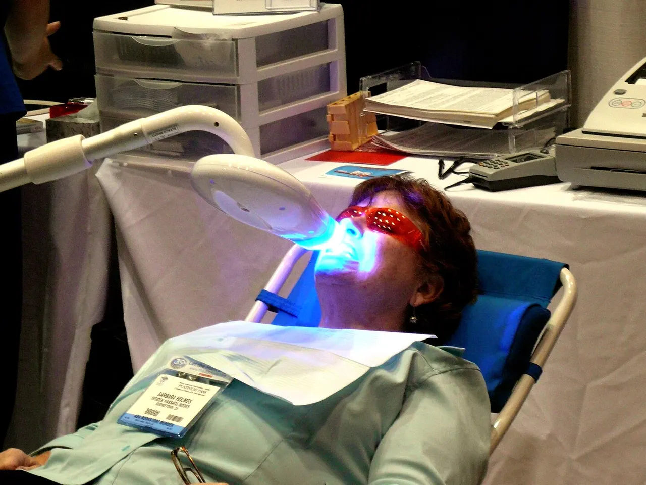 A patient in a dental chair wearing protective glasses while a blue light shines on her teeth during in-office whitening