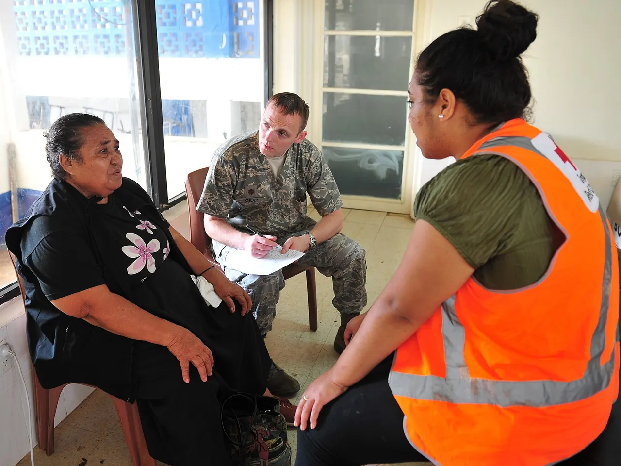 A physical therapist taking notes while talking with a patient about her knee, with another person seated beside them