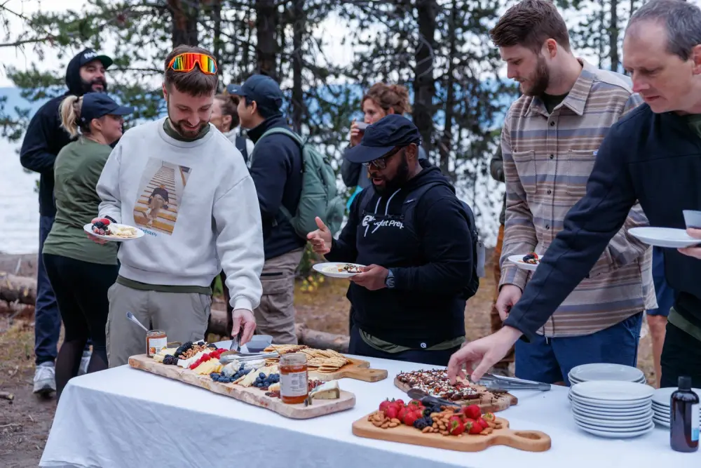 Guests serving themselves from a grazing table of cheese, fruit and dessert boards beside Paulina Lake
