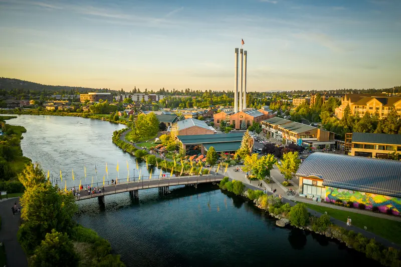 Bend’s Old Mill District at golden hour, with the three smokestacks, the Deschutes River and the footbridge
