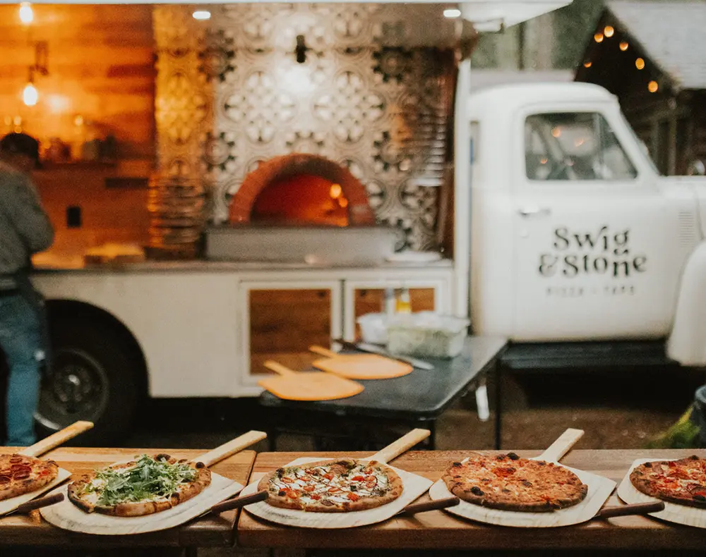 Wood-fired pizzas lined up in front of Swig & Stone’s white 1953 Ford pizza truck