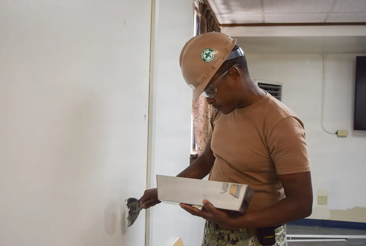 A worker spreading joint compound over a drywall patch with a taping knife