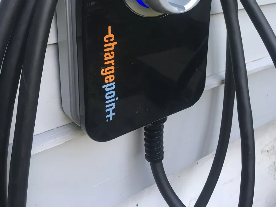 A black ChargePoint home EV charger with its cable coiled, mounted on house siding