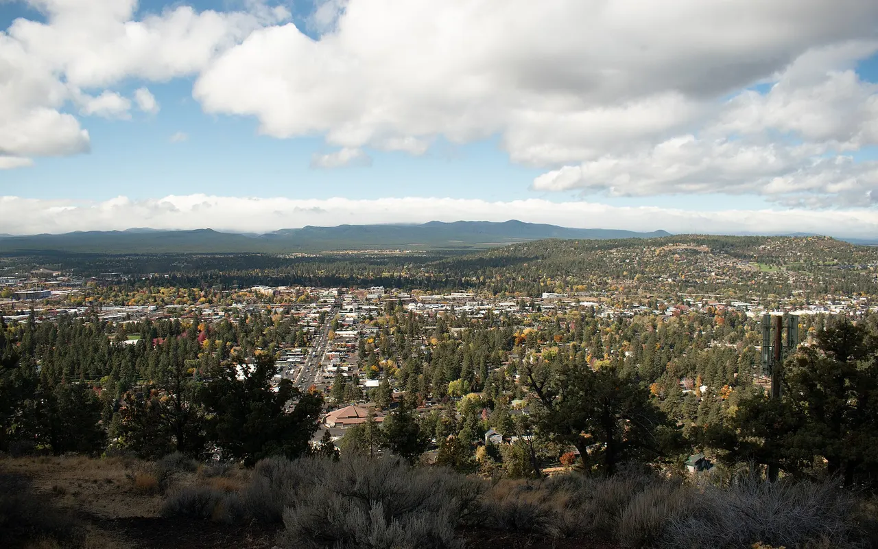 Bend’s neighborhoods and downtown under fall color, seen from the top of Pilot Butte with forested hills beyond