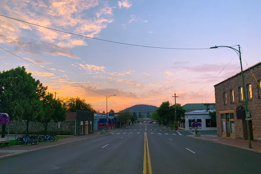 Greenwood Avenue in downtown Bend at sunrise, with old stone buildings and Pilot Butte at the end of the street