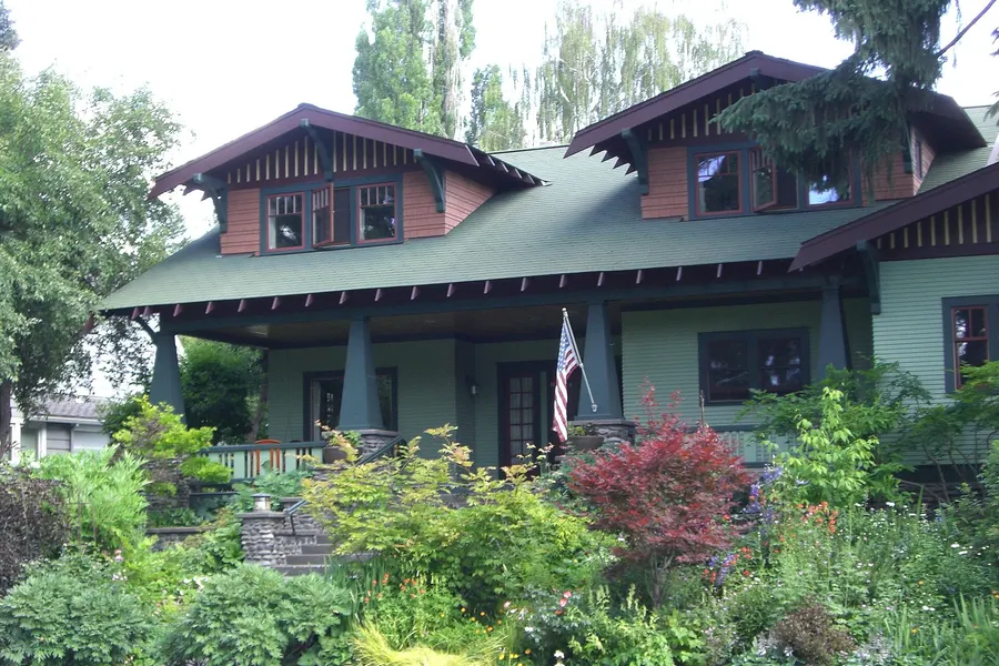 A green Craftsman bungalow with dormers, a deep porch and a flowering front garden in Bend’s Drake Park neighborhood