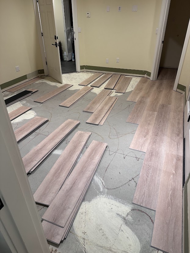 Bedroom with carpet removed, patched subfloor, and LVP planks laid out before installation