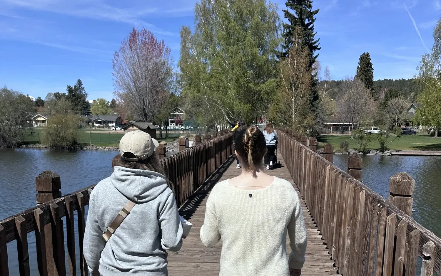 Two people walking across the wooden footbridge at Drake Park in Bend on a sunny spring day