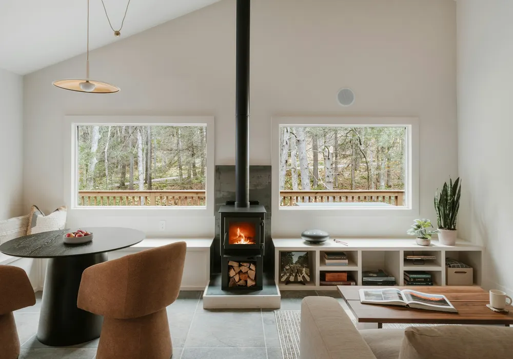 Small modern wood stove on a raised hearth in a bright room with big windows