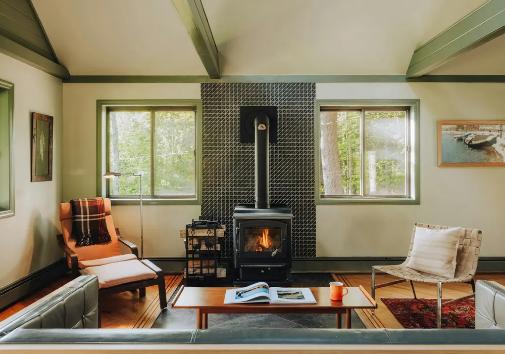 Black wood stove on a tiled wall in a bright living room with armchairs