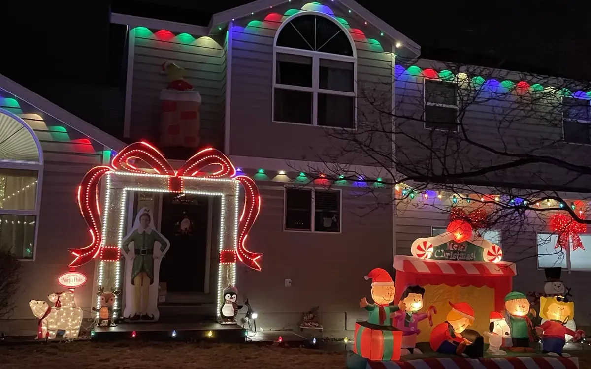 Bend two-story house at night with color C9 bulbs along every roofline, a lit gift-box arch over the front door and inflatables on the lawn