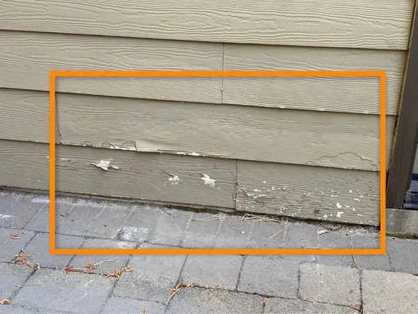 Fiber cement siding with paint flaking off along the bottom courses next to pavers