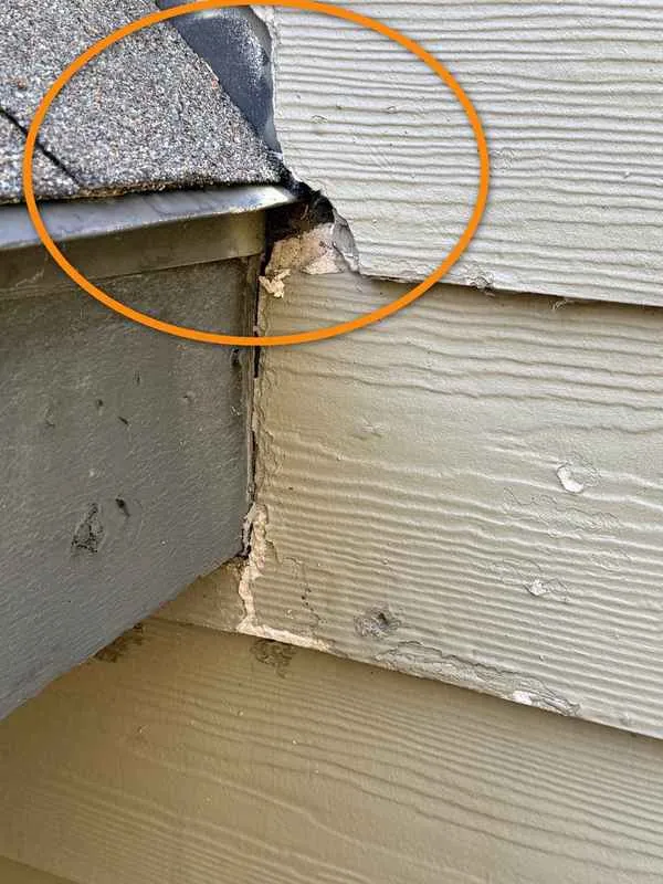 Close-up of a gap and broken siding where the roof edge meets the wall without kick-out flashing