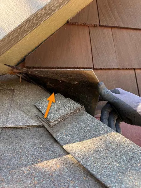 Gloved hand lifting a loose shingle at a low spot on the roof edge