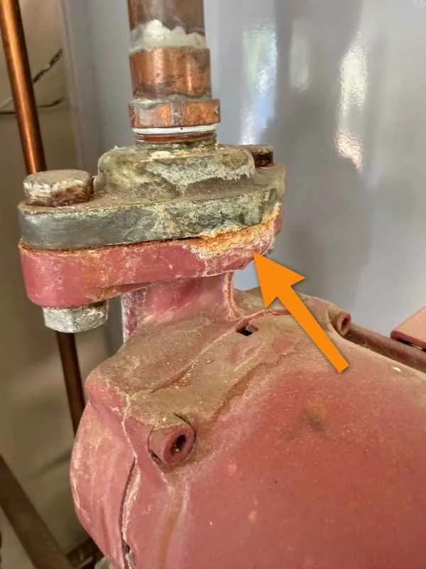 Corroded red hot water recirculation pump fitting with mineral deposits