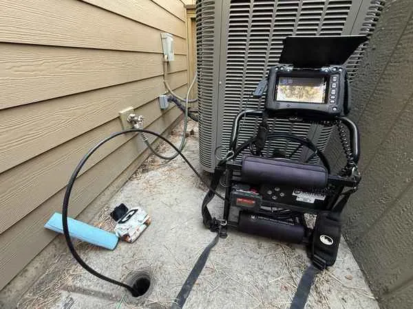 Sewer scope camera reel and monitor set up at an exterior cleanout beside a heat pump