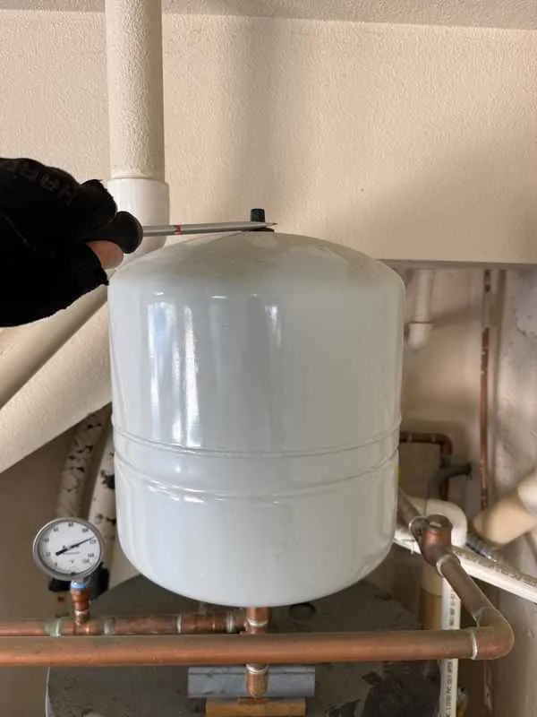 Gray expansion tank on the water heater piping in a garage