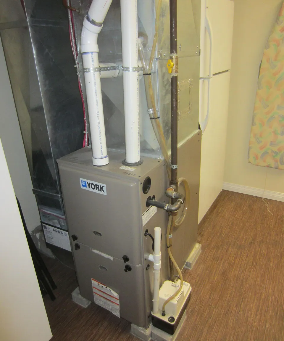 A York condensing gas furnace in a utility room with white PVC intake and exhaust pipes and metal supply and return ducts