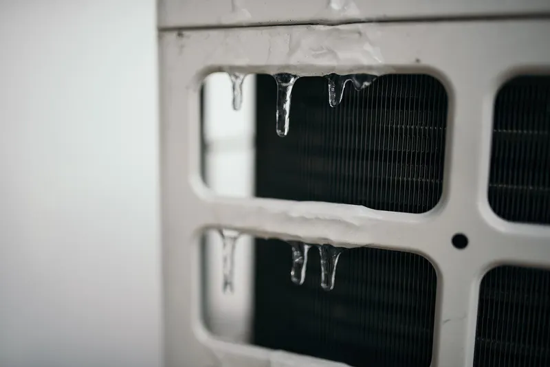 Icicles hanging from the grille of a heat pump outdoor unit in winter