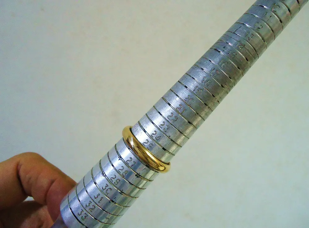 A gold wedding band slid onto a steel ring-sizing mandrel marked with size graduations