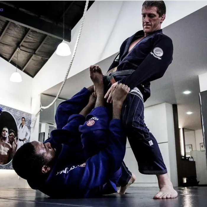 A black belt in a navy gi standing in an opponent’s open guard at Connection Rio