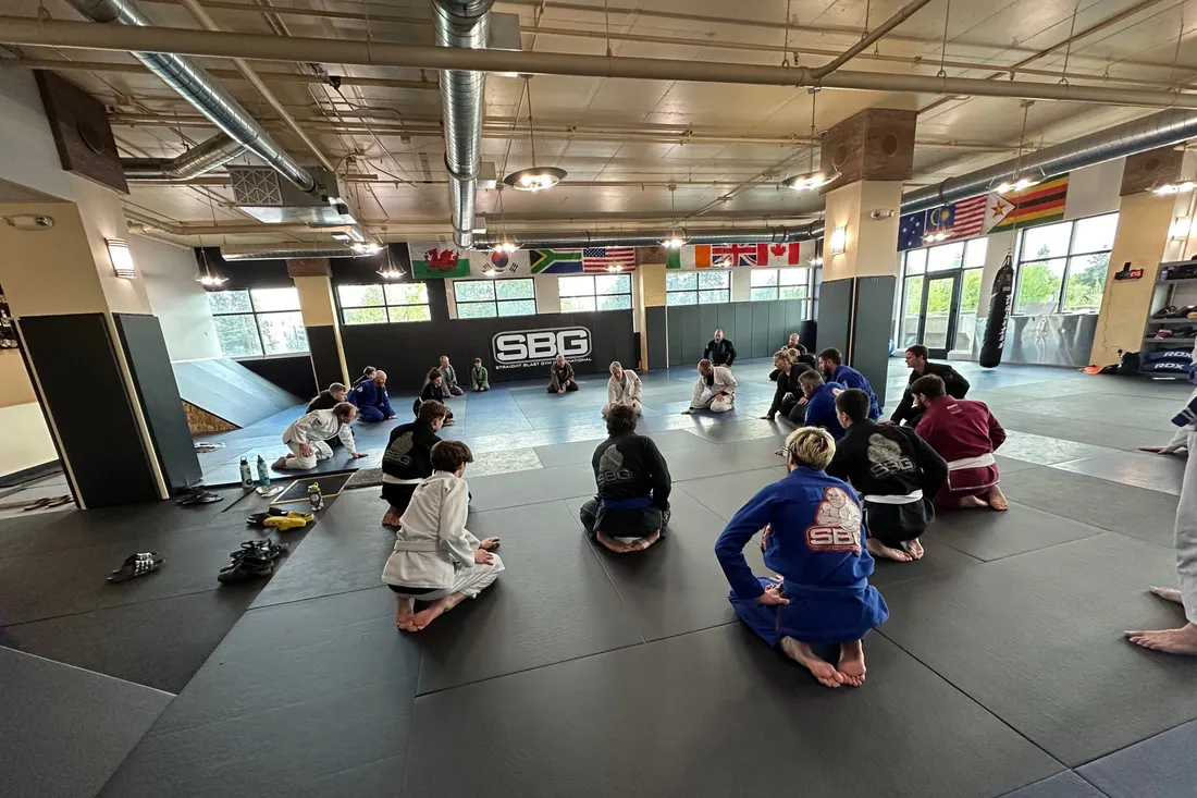 Students in gis stretching across the wide black mats of SBG Bend’s downtown gym under international flags