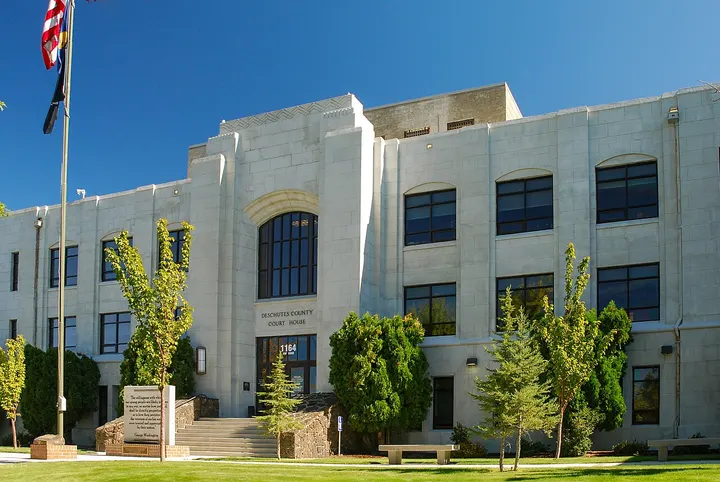 The white Deschutes County Courthouse building on NW Bond Street in Bend, with trees and a flagpole in front