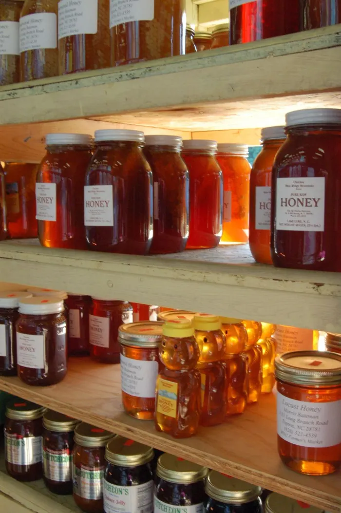 Shelves of amber honey jars with handwritten labels at a farmers market stall