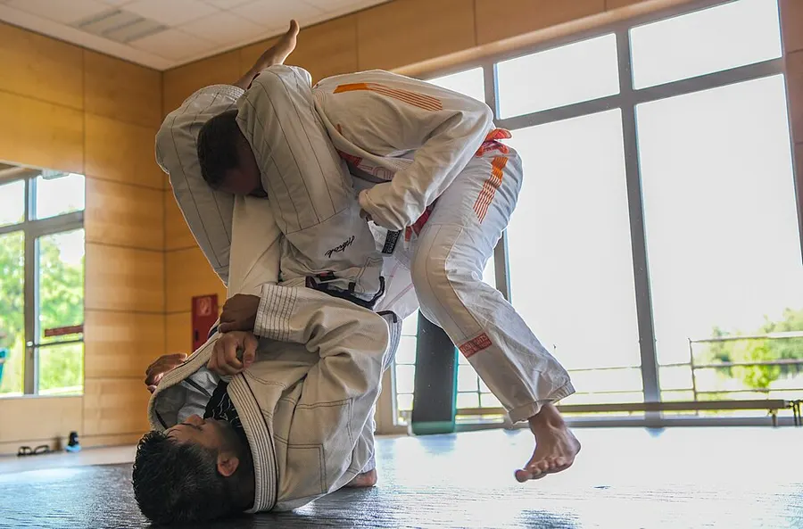 Two men in white gis grapple on a mat during a Brazilian jiu-jitsu match