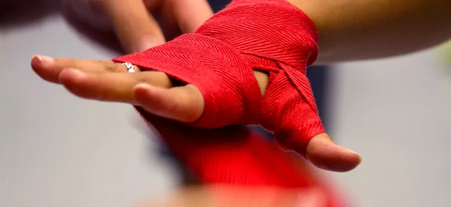 Close-up of a boxer’s hand being wrapped in red cloth hand wraps