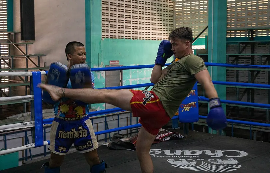 A Marine throws a roundhouse kick into a Thai trainer’s kick pads in a Muay Thai gym ring